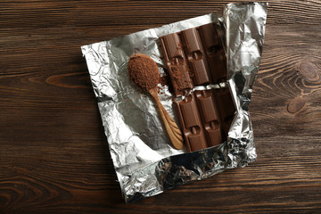 Bar of chocolate with cocoa on foil on wooden background