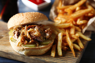 Tasty burger and french fries on plate, on wooden table background. Unhealthy food concept