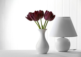 Beautiful violet tulip in vase with lamp on light background