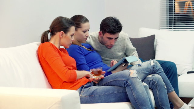 Group of friends talking over tablet on sofa at home
