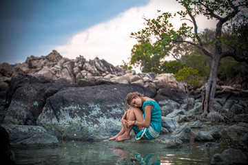 Fototapeta premium Young beautiful woman in long turquoise dress sitting on a stone