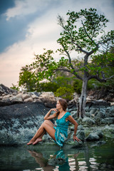 Young beautiful woman in long turquoise dress sitting on a stone