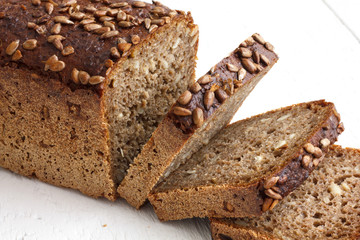 Square sunflower seed loaf sliced on rustic white surface.