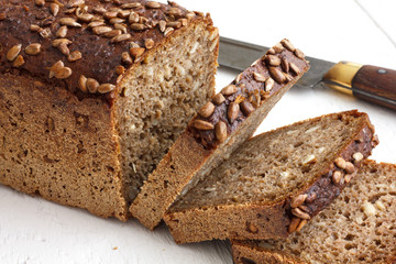 Square sunflower seed loaf sliced on rustic white surface.