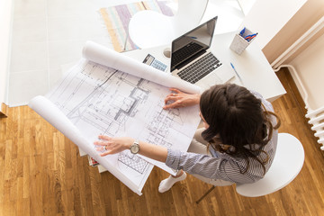 Female architect working at home.She looking at blueprint. - obrazy, fototapety, plakaty