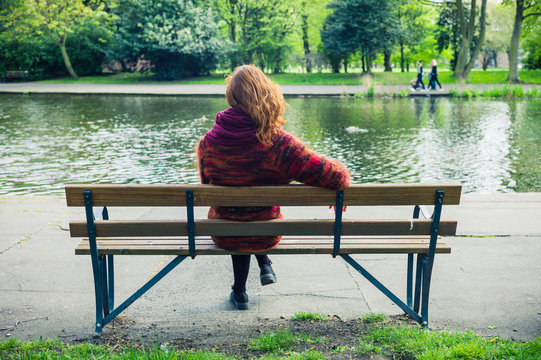 Woman sittng on bench by a pond in the park