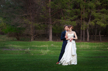 Happy bride and groom walking on the edge of a pine forest in th
