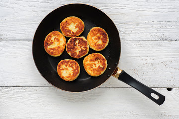 Cottage cheese pancakes in frying pan on wooden background