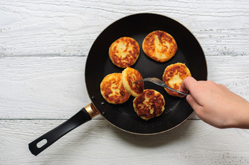 Cottage cheese pancakes in frying pan on wooden background