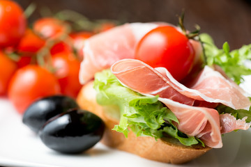 thin slices of prosciutto with olives and tomato on bread