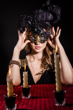 Mysterious woman in a mask near the table with alight candles