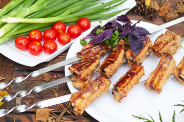 Three skewers with grilled ribs lie on a white plate with cherry
