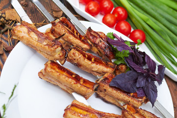 Three skewers with grilled ribs lie on a white plate with cherry
