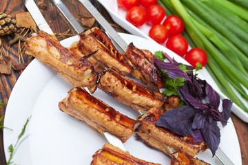 Three skewers with grilled ribs lie on a white plate with cherry
