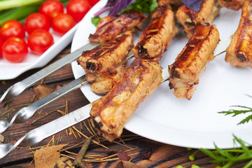 Three skewers with grilled ribs lie on a white plate with cherry