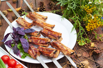 Three skewers with grilled ribs lie on a white plate with cherry