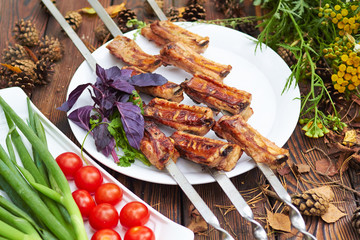 Three skewers with grilled ribs lie on a white plate with cherry