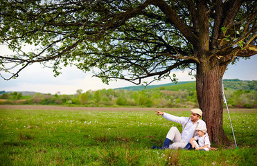 farmer father and son sitting under the tree, spring countryside