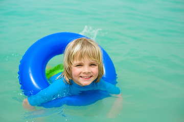 Happy little boy  with blue life ring has fun in the water