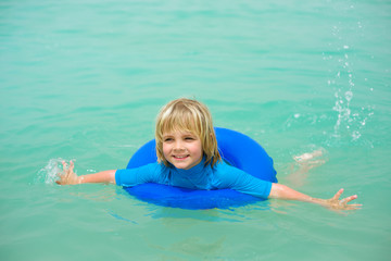 Smiling little boy  with blue life ring has fun in the water