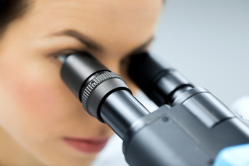 close up of scientist looking to microscope in lab