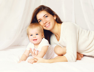 Fototapeta na wymiar Portrait of happy smiling young mother and cute baby on the bed