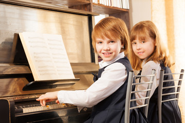 Cheerful beautiful small girls play piano together