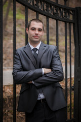 The groom or man  stand near iron gate  in autumn park