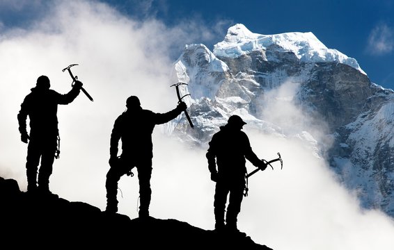 Silhouette of men with ice axe in hand and mountains
