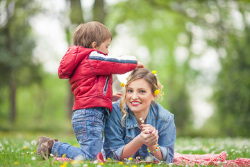 Cute little boy doing his mother's hair in a park