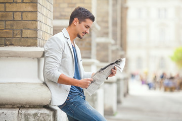 Young man reading newspaper on the city street