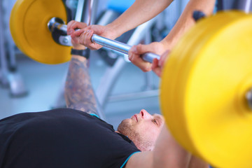 Fototapeta premium Young man lifting the barbell in gym with instructor