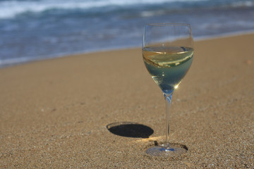 A glass of white wine in the sand on the beach. Horizontal
