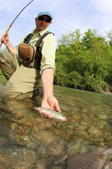 Fisherman catching brown trout with fishing line in river