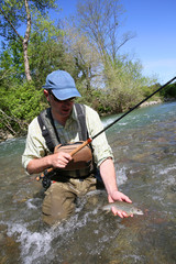 Fisherman in river catching brown trout