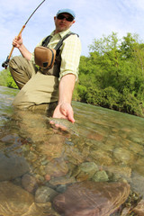 Fisherman catching brown trout with fishing line in river