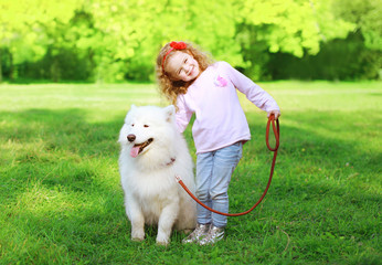 Happy child with white Samoyed dog on the grass in sunny summer