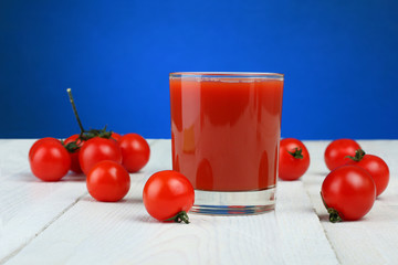 A glass of tomato juice and fresh tomatoes on a wooden table
