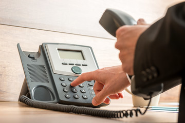 Businessman hand holding a landline telephone receiver dialing a