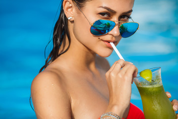 Elegant young woman in the pool with a cocktail.