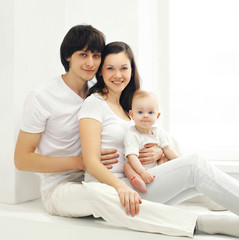 Fototapeta na wymiar Family portrait of happy parents and baby at home in white room