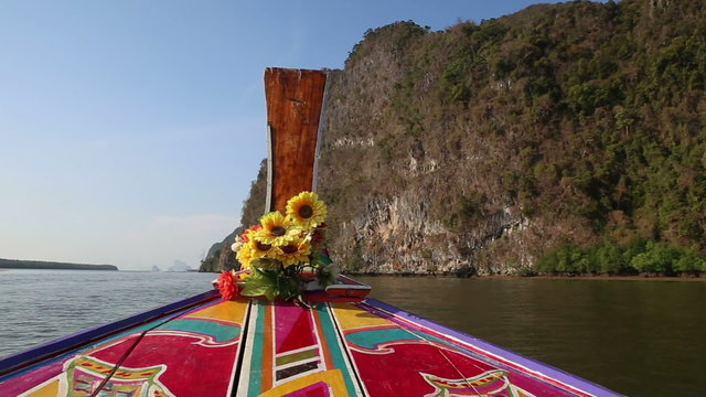 ornamented and decorated longtail boat sails up to cliffs