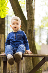 Little cute boy sitting on a tall bench in a park