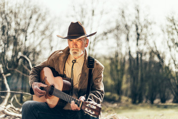 Fototapeta premium Elderly musician sitting strumming a guitar
