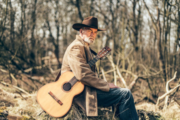 Retired elderly man sitting outdoors with a guitar