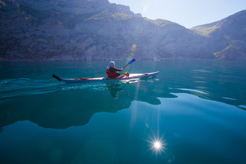 Kayak. People kayaking in sea with calm blue water near mountain