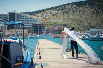 Bride and groom with a long veil go on the pier