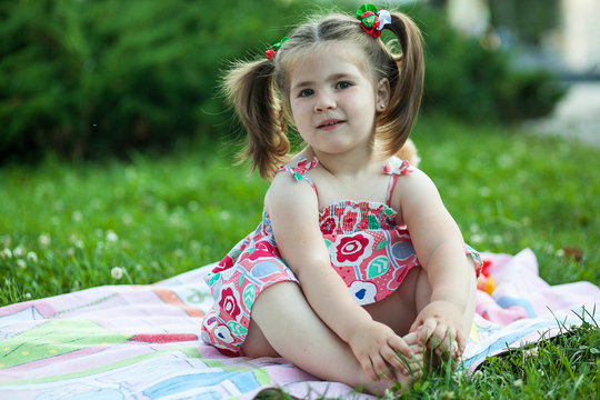 little chubby girl sitting on a mat in nature among flowers