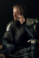 Ancient knight in metal armor talking on mobile phone