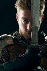 Ancient knight in metal armor with sword on gray background